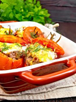 Tomatoes stuffed with meat and rice with cheese in a brazier on a towel, parsley, dill and garlic on a wooden board background