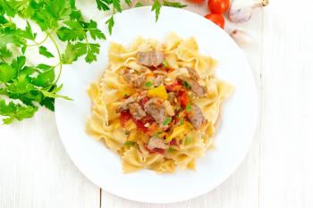 Macaroni Farfalle with turkey meat, tomato, yellow sweet pepper with sauce in a plate on the background of a wooden board from above