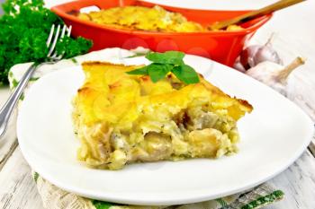 Casserole from mashed potatoes with fish fillets in a plate on a napkin on a light wooden board background