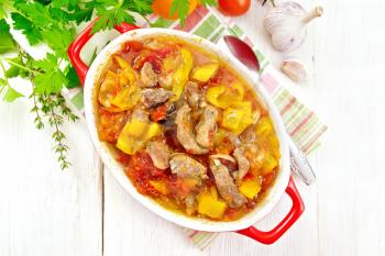 Ragout of turkey meat, tomatoes, yellow sweet pepper and onions with sauce in a brazier on a napkin on a wooden board background on top