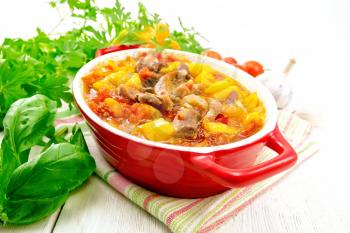 Ragout of turkey meat, tomatoes, yellow sweet pepper and onions with sauce in a red brazier on a towel on the background of a wooden board