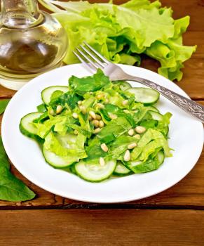 Salad from spinach, fresh cucumbers, rukkola salad, cedar nuts and spring onions, seasoned with vegetable oil and spices with a fork on a plate on the background of the board