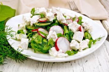 Salad with spinach, cucumbers, radish and salted cheese, dill and green onions in a bowl, towel on the background of a light wooden board