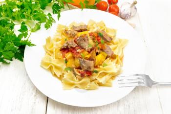Macaroni Farfalle with turkey meat, tomato, yellow sweet pepper with sauce in a plate on the background of a wooden board