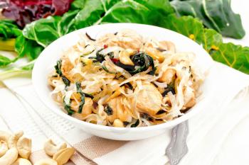 Rice noodles with leafy beet, chicken breast, cashew nuts and soy sauce in a bowl on towel on wooden plank background