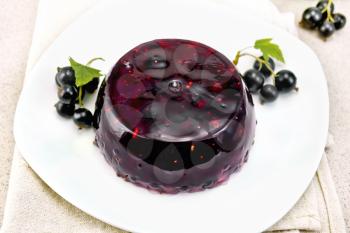 Jelly from black currant with berries in a plate on a napkin on the background of a stone table