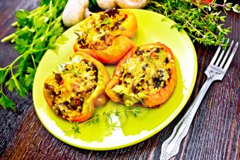 Pepper sweet, stuffed with mushrooms, tomatoes, couscous and cheese in a green plate on napkin, a fork, parsley and thyme against the background of wooden board