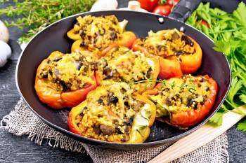 Pepper sweet, stuffed with mushrooms, tomatoes, couscous and cheese in an old frying pan on burlap, a fork, garlic, parsley and thyme against the background of a wooden board