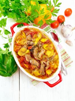 Ragout of turkey meat, tomato, yellow sweet pepper and onion with sauce in a brazier on a towel on the background of a wooden board from above