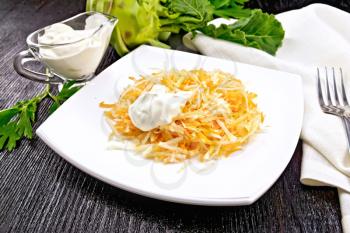 Salad of fresh carrots, kohlrabi cabbage with sour cream in a plate, napkin and fork on black wooden board background