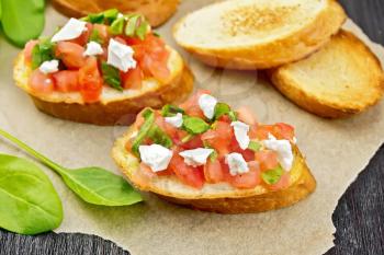 Bruschetta with tomato, spinach and soft cheese on parchment on wooden board background