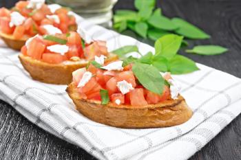 Bruschetta with tomato, basil and soft cheese on a towel on wooden board
