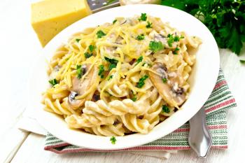 Fusilli pasta with champignons in creamy sauce, parsley and grated cheese in a dish on kitchen towel on wooden board background