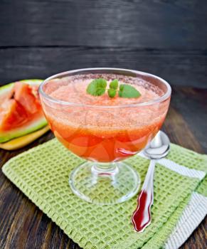 Jelly airy watermelon with mint in a glass bowl, spoon on a green towel on a background of a dark wooden board