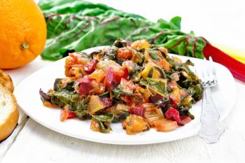 Warm chard salad with orange and onion in a plate, bread, fork on a light wooden board background