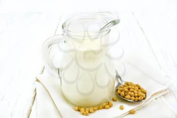 Soy milk in a jug, soybeans in a spoon on a napkin against the background of a light wooden board