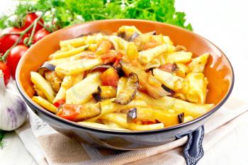 Penne pasta with eggplant and tomatoes in a bowl on towel, fork, garlic and parsley on a wooden plank background