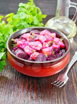 Salad of beets and potatoes, seasoned with vegetable oil and vinegar in a bowl, parsley, fork on a wooden board background