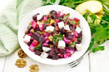 Salad with beets, salted feta cheese, apples, walnuts, parsley, seasoned with balsamic vinegar and olive oil in a plate, a towel against a wooden board
