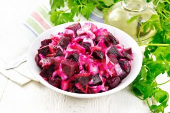 Vinaigrette salad with pickled or sauerkraut, potatoes, beetroot and onions, seasoned with vegetable oil in a bowl, napkin, parsley on the background of a light wooden board

