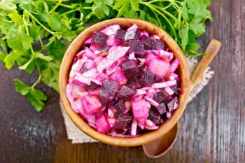Vinaigrette salad with pickled or sauerkraut, potatoes, beetroot and onion, seasoned with vegetable oil in a bowl on burlap, parsley on a wooden background from above