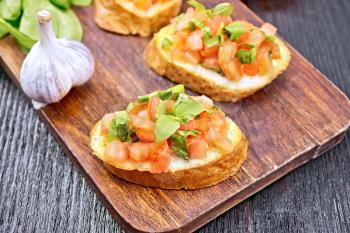 Bruschetta with tomato, basil and spinach on a plate, garlic and fresh green leaves on a wooden board background