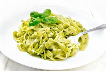 Tagliatelle pasta with pesto, basil and fork in a plate on a napkin against the background of light wooden board
