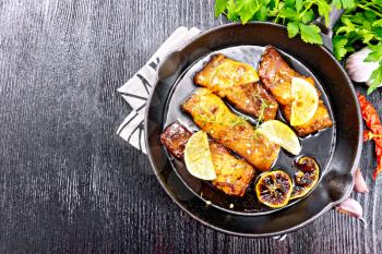 Pink salmon with honey, lemon juice, garlic, hot pepper and soy sauce, lemon slices and a sprig of thyme in a frying pan on a napkin, parsley on wooden board background from above
