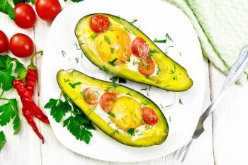 Scrambled eggs with cherry tomatoes in two halves of avocado in a plate, napkin and fork on the background of a light wooden board from above