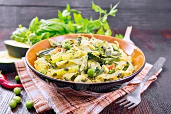 Tagliatelle pasta with zucchini, green peas, asparagus beans, hot peppers and spinach in  kitchen towel, garlic, fork and basil on dark wooden board