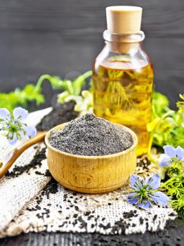 Flour of black caraway in a bowl, seeds in a spoon burlap, oil in bottle and twigs Nigella sativa with blue flowers and leaves on wooden board background
