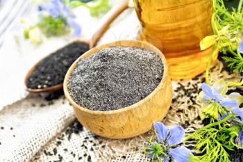 Flour of black caraway in a bowl, seeds in a spoon burlap, oil in bottle and twigs Nigella sativa with blue flowers and green leaves on wooden board background