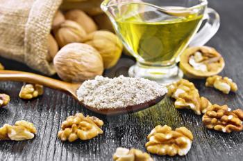 Walnut flour in a spoon, nuts on a table and in bag, oil in a glass sauceboat on background of dark wooden board