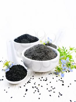 Flour and seeds of black caraway in bowls, sprigs of kalingini with blue flowers and green leaves on a background of light wooden board