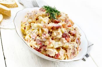 Salad with chicken, sweet pepper, tomato, egg and cheese seasoned with mayonnaise and garlic in a dish, napkin, bread and forks on a wooden board background