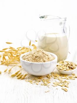 Flour oat in bowl, milk in a jug, oatmeal in spoon, oaten stalks on the background of wooden table
