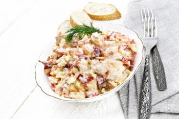 Salad with chicken, sweet pepper, tomato, egg and cheese seasoned with mayonnaise and garlic in a dish, napkin, bread and forks on a white wooden board background
