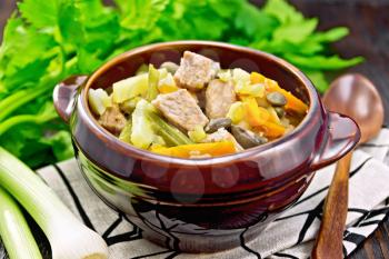Eintopf soup made from pork, celery, beans, carrots and potatoes with leek in a clay bowl on a napkin on wooden board background