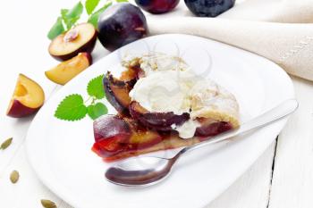 Piece of sweet pie with plum, sugar, cardamom and ice cream in a plate, sprigs of green mint, a napkin on wooden board background