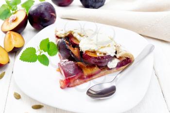 Piece of sweet pie with plum, sugar, cardamom and ice cream in a plate, sprigs of green mint, towel on wooden board background