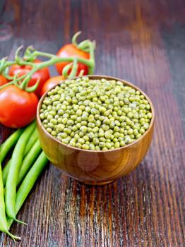 Green lentils mung in a bowl, pods of beans and red tomatoes on a wooden board background