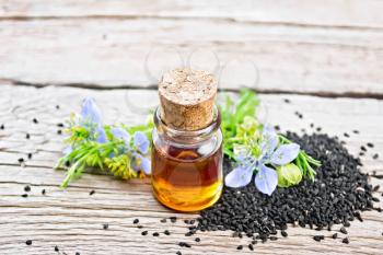Nigella sativa oil in a bottle, seeds and twigs of black caraway seeds with blue flowers and green leaves on a background of an old wooden board