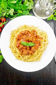 Spaghetti pasta with Bolognese sauce of minced meat, tomato juice, garlic, wine and spices in a plate, vegetable oil, spicy herb on a dark wooden board background from above