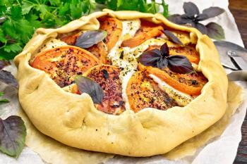 Pie with tomatoes, cottage cheese and purple basil on parchment, parsley on a wooden board background