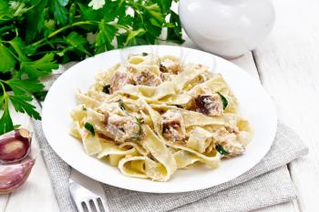 Tagliatelle pasta with salmon, cream, garlic and herbs in a plate on a towel, fork, parsley and basil on wooden board background