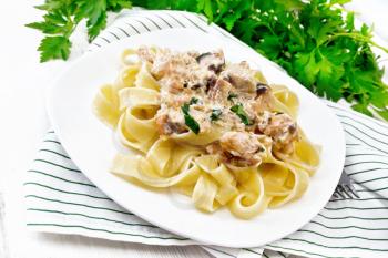 Tagliatelle pasta with salmon, cream, garlic and herbs in a plate on a towel, fork, parsley and basil on white wooden board background
