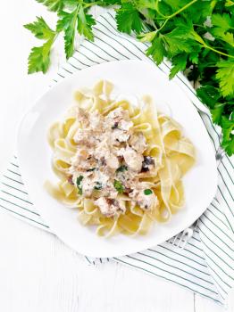 Tagliatelle pasta with salmon, cream, garlic and herbs in a plate on a towel, fork, parsley and basil on a white wooden board background from above