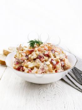 Salad with chicken, sweet pepper, tomato, egg and cheese seasoned with mayonnaise and garlic in a dish, towel, bread and forks on a white wooden board background