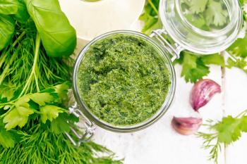 Sauce of dill, parsley, basil, cilantro, other spicy herbs, garlic and vegetable oil in a glass jar, coarse salt on wooden board background from above
