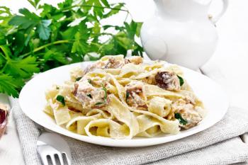 Tagliatelle pasta with salmon, cream, garlic and herbs in a plate on a napkin, fork, parsley and basil on the background of light wooden board